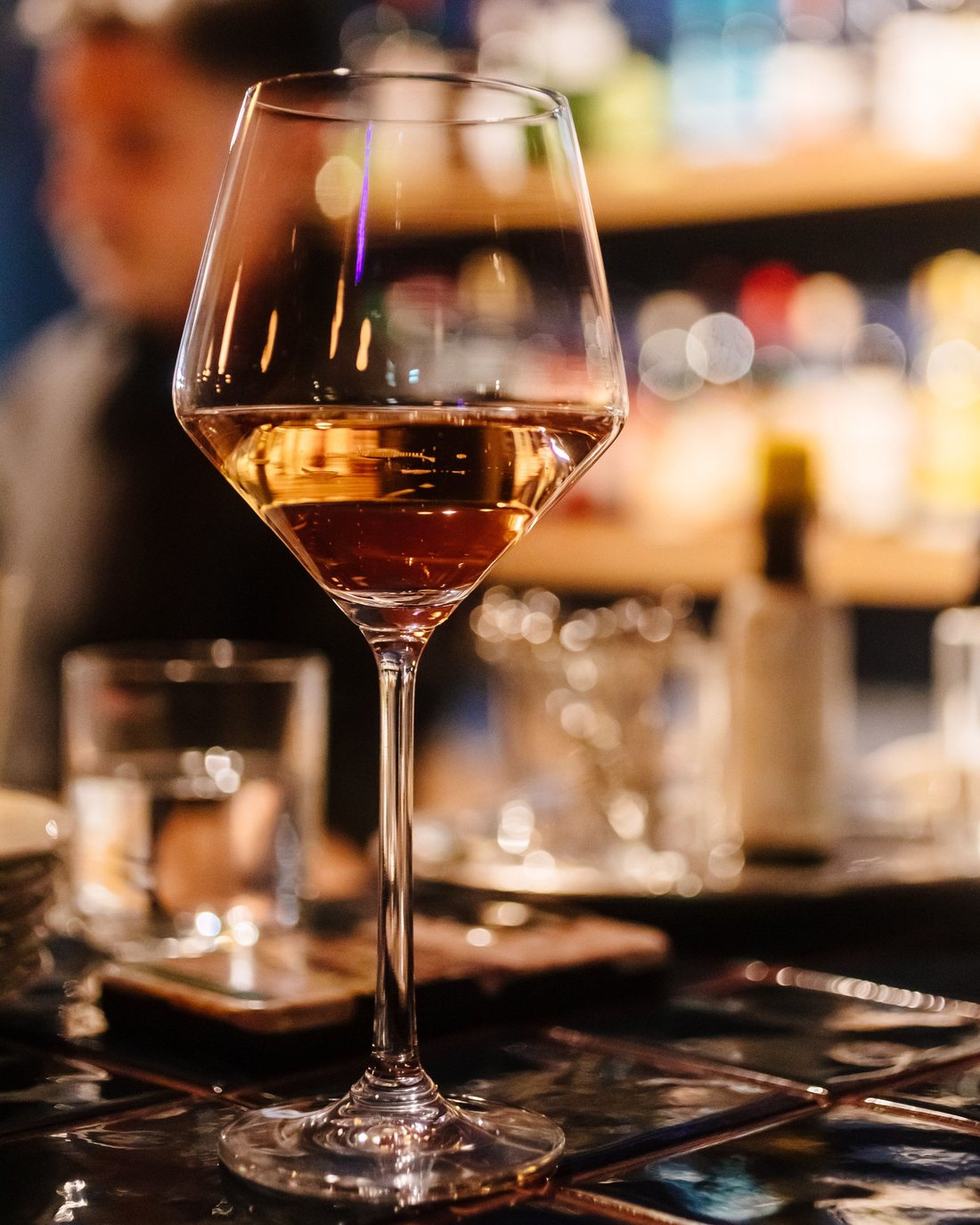 Una copa de vino sobre la barra, con las botellas del bar de fondo.